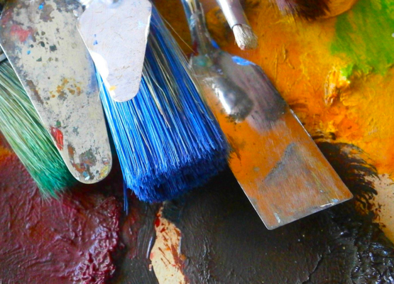 Photo of various paintbrushes and paint tools on top of a piece of art.